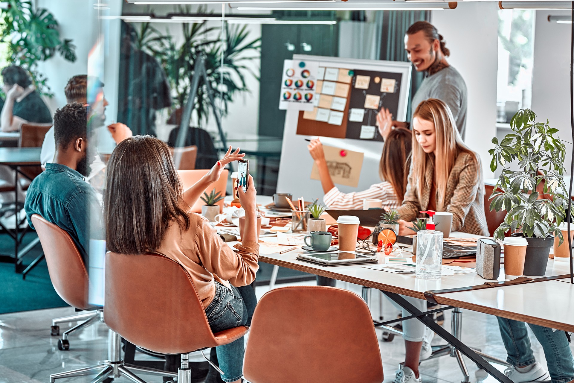 Meeting in the office, productive team of young professionals working at a large table using modern technology devices.